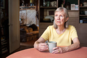 Single senior woman in yellow shirt looking over to side while holding cup indoors